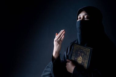 Asyalı Müslüman bir kadın ayakta ve Kuran okuyor ve Kuran 'ı takdir ediyor ve ona inanıyor. Kuran' ın Arapça kaligrafi anlamı, Arapça kelime çevirisi, Kutsal Kur 'an..