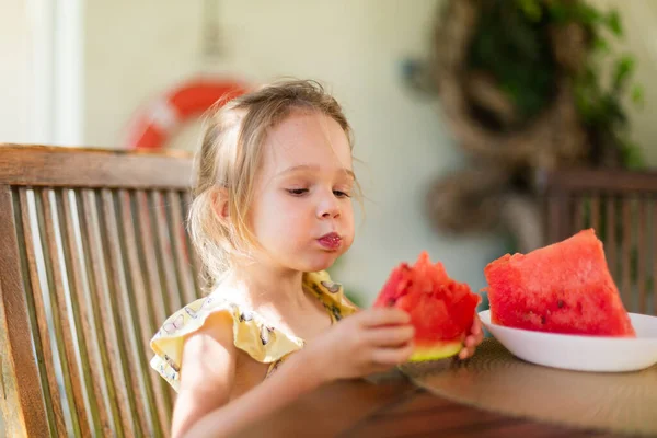 Little girl eating watermelon outside on terrace