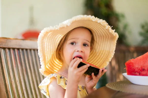 Little girl eating watermelon outside on terrace