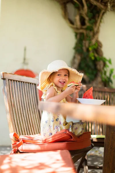 Little girl eating watermelon outside on terrace
