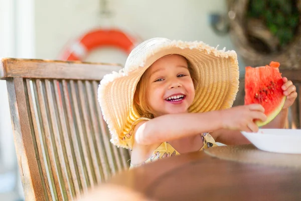 Little girl eating watermelon outside on terrace
