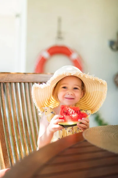 Little girl eating watermelon outside on terrace