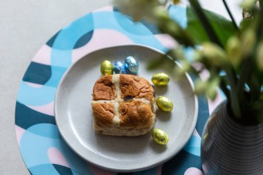 Cross bun and chocolate easter egg with eggs on a white plate