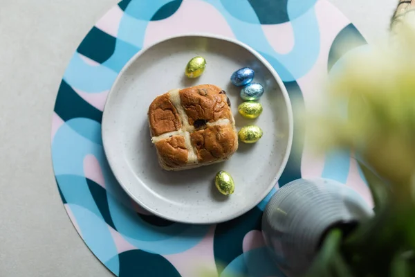 Cross bun and chocolate easter egg with eggs on a white plate