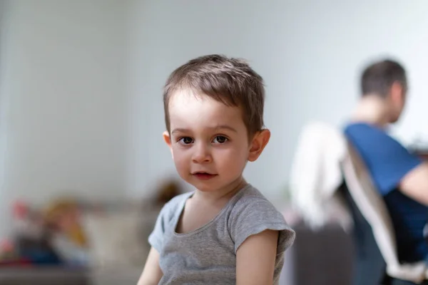 Babası arka planda çalışırken kameranın önünde duran küçük bir çocuk.
