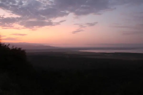 Afrika ufkunun üzerinde gün batımı gökyüzünün bozkırla buluştuğu sakin bir doğa görüntüsüyle kaybolan ışıkla.