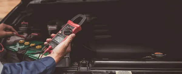 The mechanic uses a multimeter with voltage measurement to check the car voltage level.