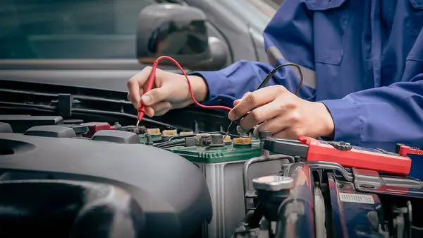 The mechanic uses a multimeter with voltage measurement to check the car voltage level.