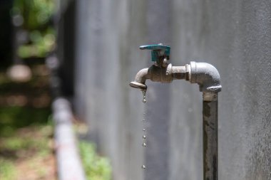Bahçeye su damlayan eski metal musluk, çimento duvarı ve doğa..