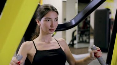 Sağlık, fitness ve vücut geliştirme konsepti. Spor salonunda kaslarını ve trisepslerini şişiren genç atletik kadın.