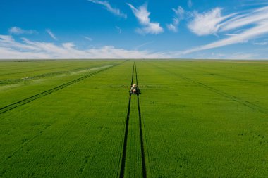 Yeşil alanda traktör sprey gübresinin havadan görünüşü. Tarım traktörü tarlayı sürüyor ve püskürtüyor..