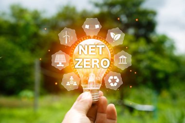 net sıfır konsepti. Bulanık yeşil yaprağın üzerinde sıfır simgesiyle el ele tutuşmak. Çevresinde temiz enerji ikonu olan karbon nötr ve yeşil doğal arka plan. Karbon gazı küresel ısınmayı etkiliyor.