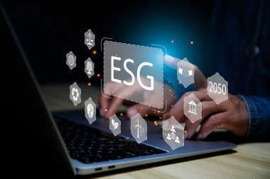 2050 yılında ESG çevre, sosyal, sürdürülebilir ve etik kavramları için veri analizi yapan bir iş adamı. Ofis arka planında ESG simgesi etrafında eko yeşil enerji sistemi simgesi