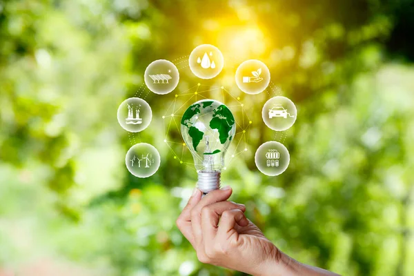 green energy concept. world icon in light bulb on hands with green nature background. green energy icon around. energy reusing for maximum benefit. ESG concept for environmental, social, ethical.