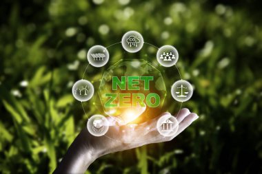 net sıfır konsepti. Bulanık yeşil yaprağın üzerinde sıfır simgesiyle el ele tutuşmak. Çevresinde temiz enerji ikonu olan karbon nötr ve yeşil doğal arka plan. Karbon gazı küresel ısınmayı etkiliyor.
