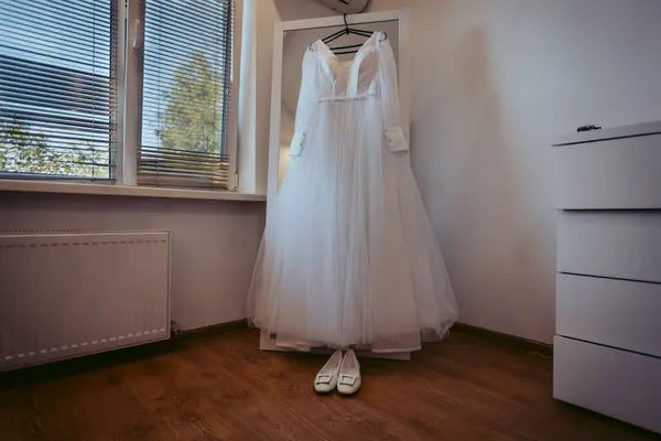 Odada asılı beyaz gelinlik ve ayakkabılar, sabah hazırlıkları.