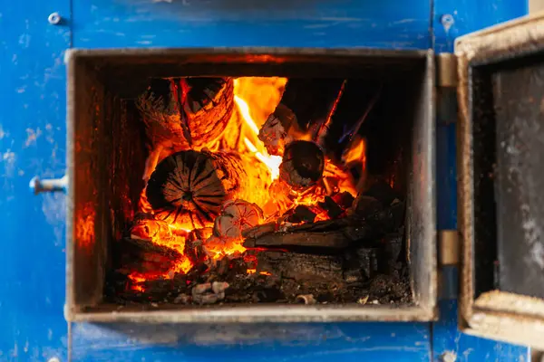Katı yakıt kazanının içinde kapı açık, yakın plan kütükler yakıyor.