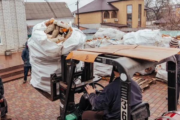 Bir forklift kamyondan büyük torbalar dolusu odun boşaltır ve bulutlu bir kış gününde onları çit boyunca yığar.