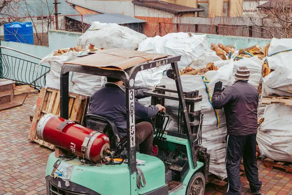 Bir forklift kamyondan büyük torbalar dolusu odun boşaltır ve bulutlu bir kış gününde onları çit boyunca yığar.