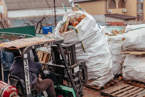 Bir forklift kamyondan büyük torbalar dolusu odun boşaltır ve bulutlu bir kış gününde onları çit boyunca yığar.
