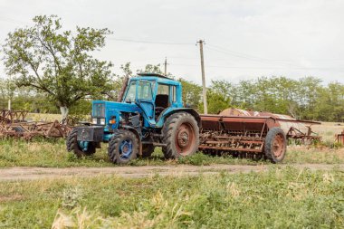 Güneşli yaz gününde tarımsal alanda karavanlı mavi traktör.