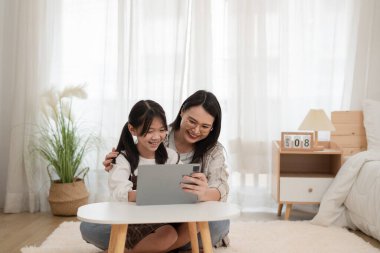Asyalı aile kadını ve kızı evde dijital tablet kullanıyorlar.