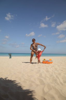 Anne ve 2 yaşındaki kızı, Karayip sahillerinde okyanus geçmişiyle mutlu poz veriyorlar.