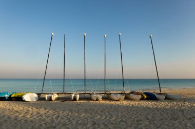 Arka planda turkuaz mavi deniz olan kumda yelkenliler.