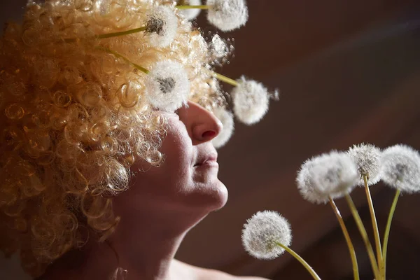 Portrait of woman in white blonde wig with dandelions. Female model posing in studio for dark picture