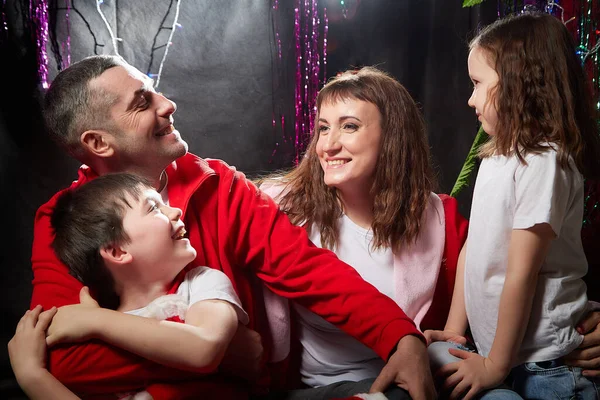 Lovely Family with mother, father, son and daughter having fun in the room derorated fot Christmas night. Children and parents posing fot phtot shoot in dress of Santa Claus