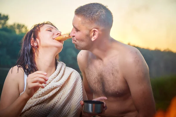 Wet happy Couple relaxin, having fun, hugs and pizza with fire in camping on nature near in summer sunny evening in sunset. Family or lovers have date and rest outdoor. Concept of love and travel