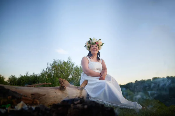 Slavic plump plump chubby girl in long white dress on the feast of Ivan Kupala with flowers on nature on summer evening