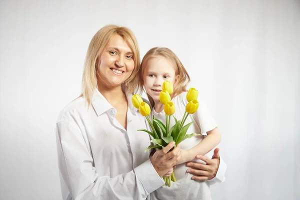 Blonde mother and daughter with a bouquet of tulips on a white background. Mom and girl together on holiday mothers day with flowers. Congratulations to women on International Womens Day on March 8