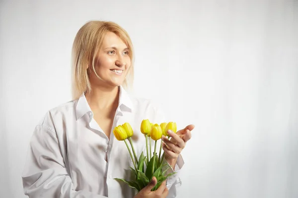Beauty young blonde happy woman with bouquet of yellow tulips on white background. The concept of holiday and a gift for a lady and a girl