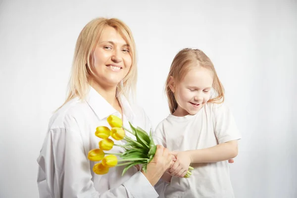 Blonde mother and daughter with a bouquet of tulips on a white background. Mom and girl together on holiday mothers day with flowers. Congratulations to women on International Womens Day on March 8
