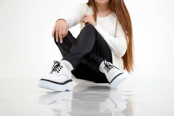 Beautiful white sneakers and woman legs in the studio on white background. Fashionable shooting of young girl with beautiful legs