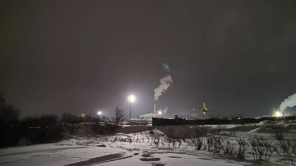 Night industrial landscape. View of large plant and snow-covered territory. Cold winter weather. Severe polar climate in the Arctic region. Industry and energy in the Far North