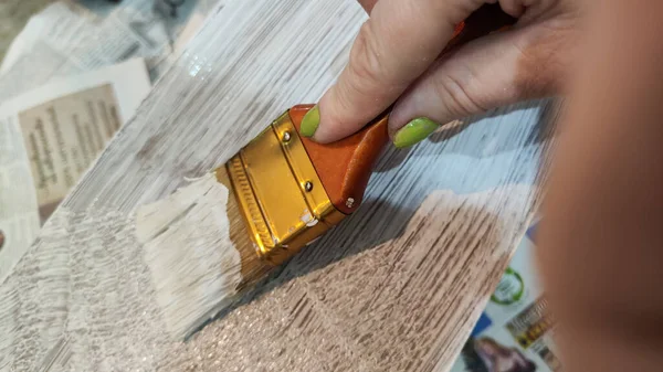Woman hand painting on wooden boards with Brush full of white paint. Painting of new wood board or furniture and old newspaper on background. Partial focus