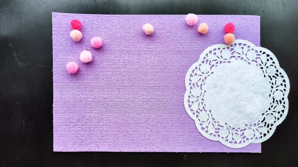 Top view of lilac or purple sheet of velvet paper, white a carved napkin and color ball. Abstract frame, background and texture with copy space. Empty rectangle with round paper napkin on black colour