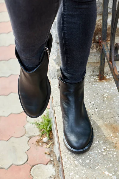 Female winter, autumn or spring black leather shoes on leg of woman outdoors. Fashionable modern photography and photoshoot on the street for store, catalog, magazine or online