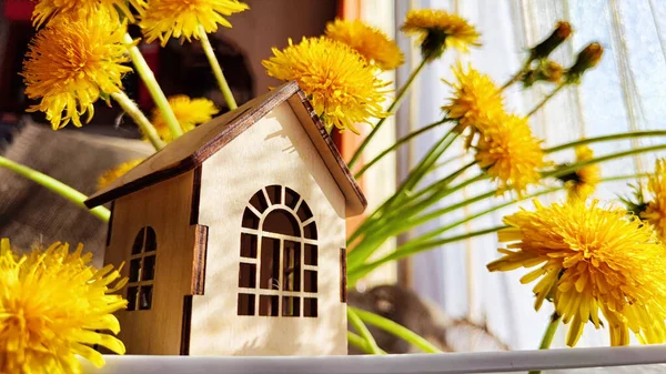 miniature toy house in grass and dandelion flowers, spring natural background. symbol of family. mortgage, construction, rental, property concept. Eco Friendly home. soft selective focus. copy space