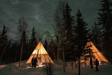 Kuzey Işıkları (Aurora Borealis), Kanada 'nın Kuzeybatı Bölgesi, Yellowknife yakınlarındaki ormanlarda aydınlatılmış çadırlar.
