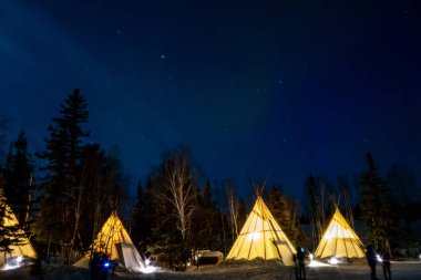 Kuzey Işıkları (Aurora Borealis), Kanada 'nın Kuzeybatı Bölgesi, Yellowknife yakınlarındaki ormanlarda aydınlatılmış çadırlar.