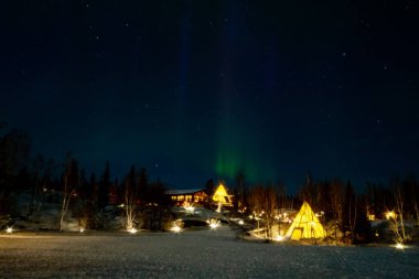 Kuzey Işıkları (Aurora Borealis), Kanada 'nın Kuzeybatı Bölgesi, Yellowknife yakınlarındaki ormanlarda aydınlatılmış çadırlar.