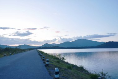 Su deposu gölündeki yol, gün batımında dağ arkaplanı.