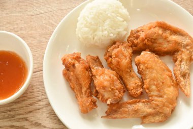 Kızarmış tavuk budu ve kanatlı biber sosu tabakta pilavla yenir.