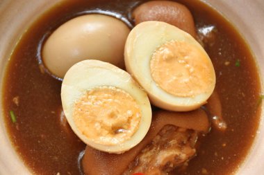 boiled half cut egg with fat pork leg in herb brown soup on bowl 