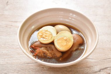 boiled half cut egg with fat pork leg in herb brown soup on bowl 