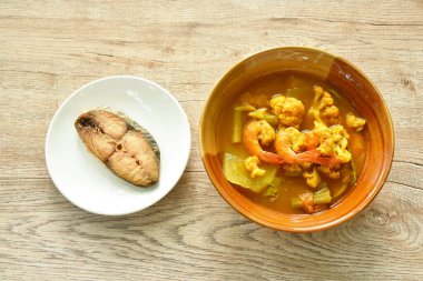 Baharatlı ve ekşi körili çorba içinde haşlanmış karides ve karışık sebze tabakta kızarmış tuzlu Hint-Pasifik kral uskumrusu yiyin. 