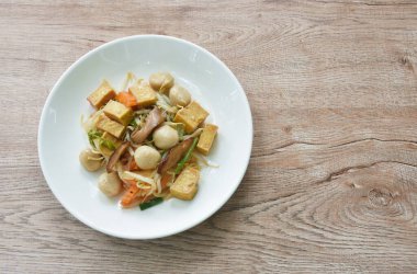 Kızarmış fasulye filizi, dilimlenmiş sarı tofu ve tabakta siyah mantar soslu balık köftesi.